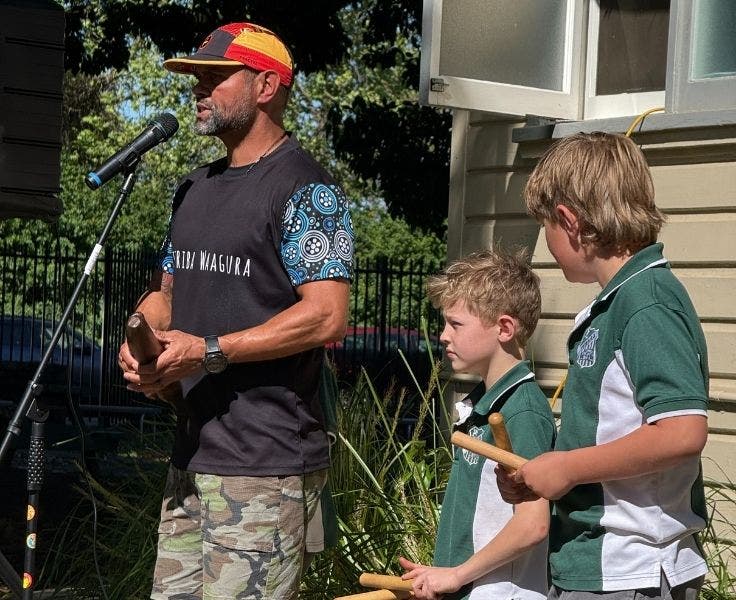 Uncle Dale singing during Corroboree with two students using clapping sticks.