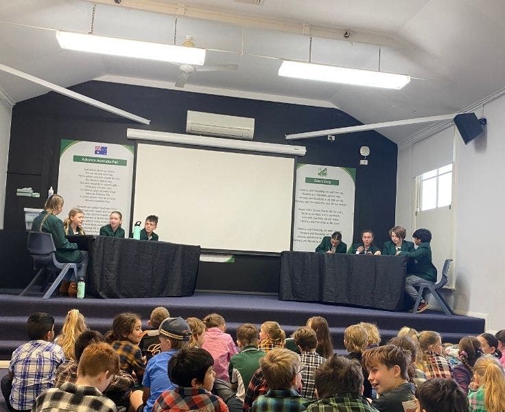 Two debating teams on the stage and the audience sitting on the floor.