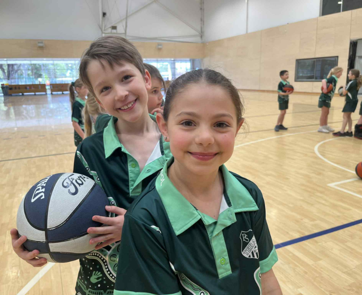 Two students smiling at the camera, one is holding a basketball.