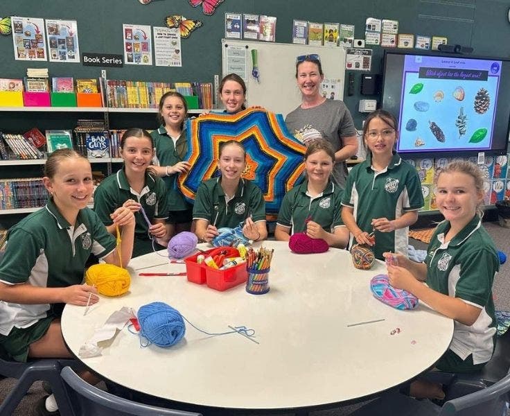 Group of students sitting at a round table crocheting.
