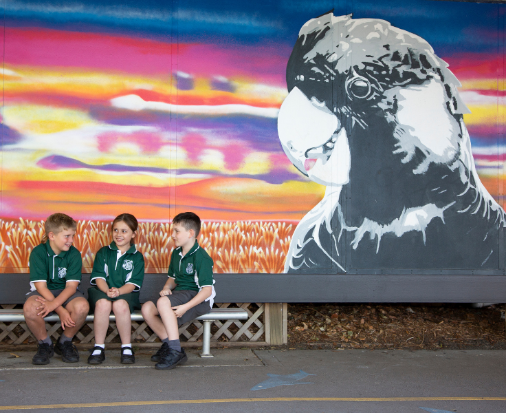Three children sitting in front of a cockatoo mural.