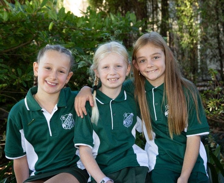Three children sitting in front of a garden.