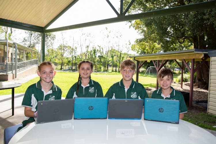 Four children on Chromebooks in an outdoor learning environment.