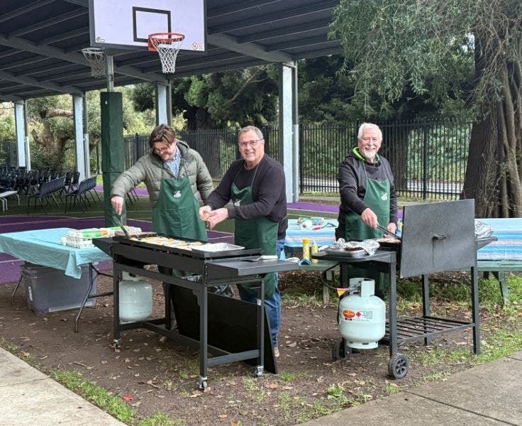 Three men cooking breakfast on two barbeques.