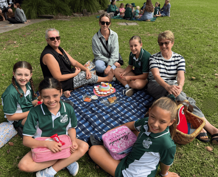 Students and families sitting together on a picnic rug.