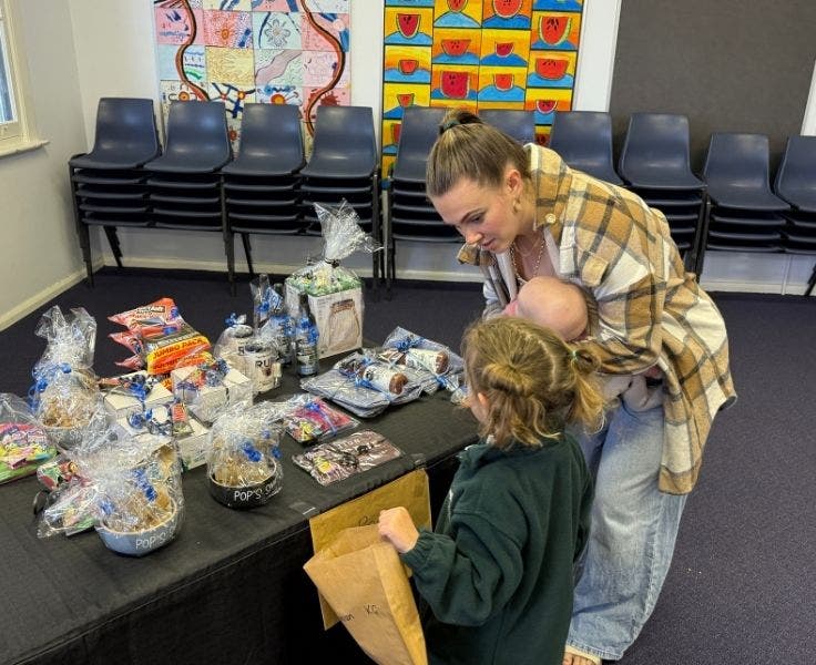 A parent volunteer holding a baby helping a student choose a Father's day gift.