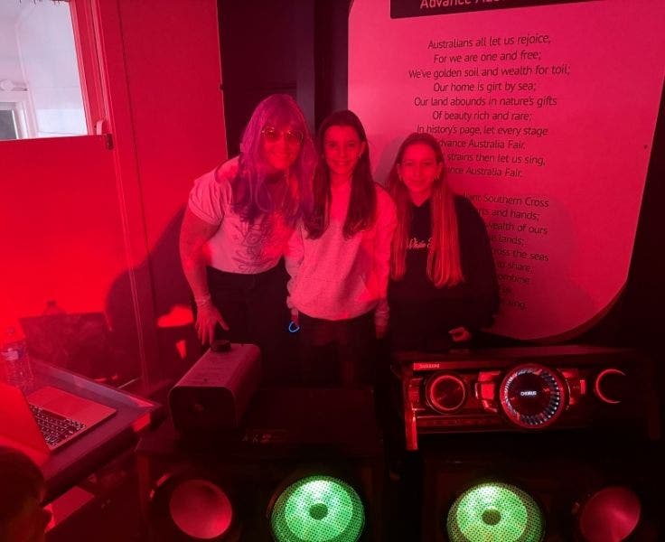 A parent volunteer DJing for the P&C disco with two students.